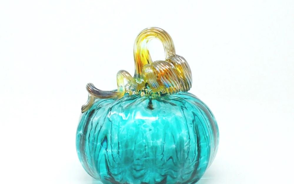 A hand-blown teal glass pumpkin with a curling amber stem.